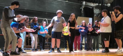 The cast of Anastasia hard at work blocking their movements for the press conference scene at a Saturday rehearsal. A group of reporters circle around senior Connor Farrington (center left) and sophomore Echo Picone (center right). (Photo courtesy of Sofia Schiano)