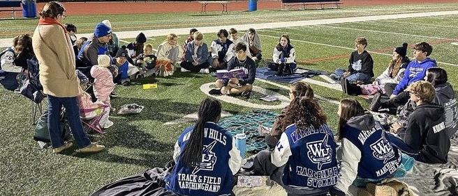 Children and high school students listen to a story at the Warren Hills Stadium’s 40-yard line during Reading Under the Stars Nov. 6. (Photo courtesy of Heather Wight)
